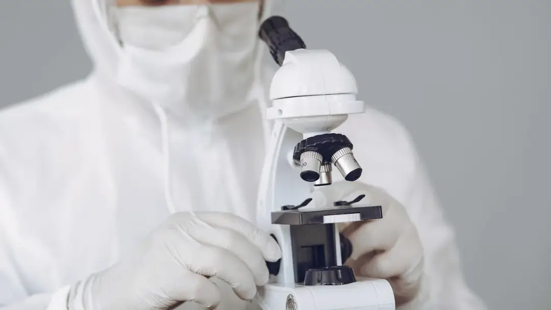 Profesional de laboratorio con traje de protección observando una muestra en un microscopio